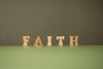 Word FAITH made of wooden letters on a green background. 