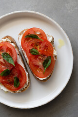 Breakfast toasts with cream cheese, fresh tomato, olive oil and baby spinach on a white plate. Healthy tasty food concept, top view