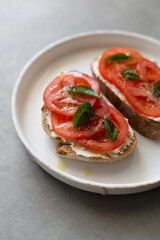 Breakfast toasts with cream cheese, fresh tomato, olive oil and baby spinach on a white plate. Healthy tasty food concept, top view