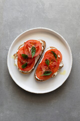 Breakfast toasts with cream cheese, fresh tomato, olive oil and baby spinach on a white plate. Healthy tasty food concept, top view