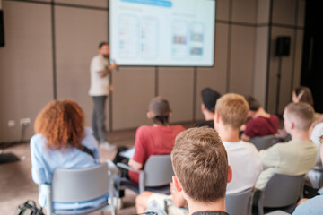 Group of people seated in lecture hall attentively listening to presentation by speaker. Educational environment promotes learning and engagement.