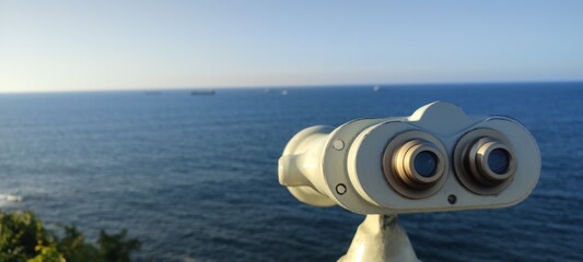 Binocular viewer overlooking the ocean with ships in the distance