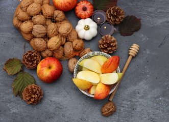 Fototapeta premium Autumn still life with apples, nuts, red leaves and candles on a table. Textured background with space for text. 