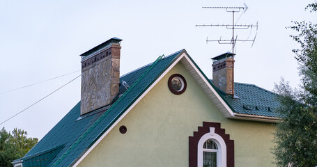 A green-roofed house features stone chimneys under a clear sky in a quiet residential area