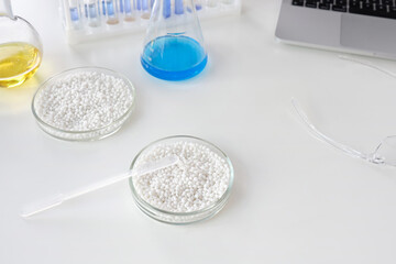 Laboratory Petri dishes with white granules on a background of chemical tools and glassware and laptop.