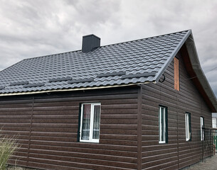 Close-up house roof with steel roofing sheet. Dark modular tile effect roof panel. Traditional metal shingle tiles. Profiled metallic corrugated pantile as clay or concrete slate. Building's covering