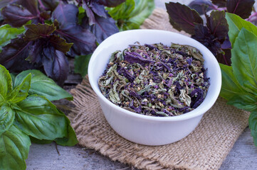 Dried basil in a bowl and fresh basil leaves on a wooden background. Green and purple basil..