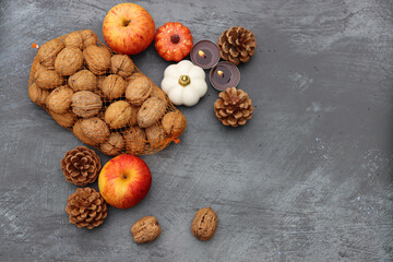 Autumn background. Apples, nuts, fir cones, candles and autumn leaves on dark textured table with space for text.  