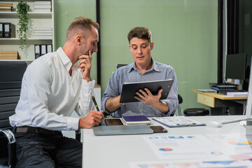Caucasian middle-aged male businessperson and an Italian accountant are seated at a desk, engaging in a professional meeting, discussing various aspects of technology and innovation in their fields.
