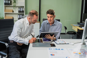 Caucasian middle-aged male businessperson and an Italian accountant are seated at a desk, engaging in a professional meeting, discussing various aspects of technology and innovation in their fields.