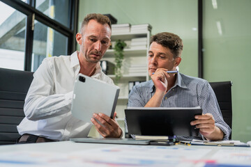 Caucasian middle-aged male businessperson and an Italian accountant are seated at a desk, engaging in a professional meeting, discussing various aspects of technology and innovation in their fields.