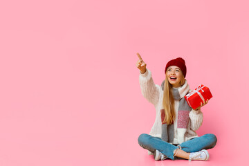 Time to buy christmas gifts. Excited girl in winter hat with gift box pointing at copy space, sitting on floor, copy space