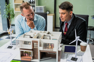 Caucasian middle-aged businessman and an Italian accountant at desk with a monitor, discussing the...