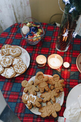 on the kitchen table on a tablecloth with New Year's decor there are gingerbread cookies in plates, preparing a gingerbread house photo with noise effect close up