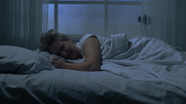 Sad woman crying while lying in bed in bedroom at night, loneliness, insomnia.