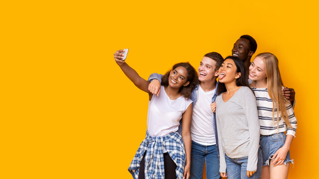 Nice time together. Cheerful group of multiethnic friends taking selfie on smartphone over yellow studio background