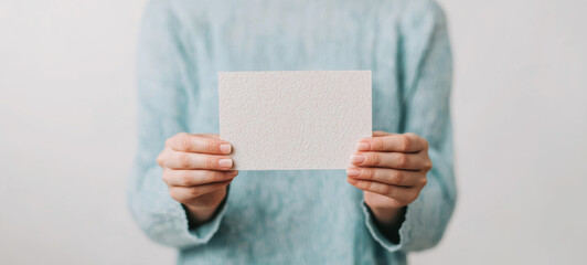 A person holding a blank card, showcasing simplicity and space for creativity in a minimalist setting.