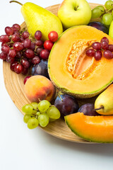 A plate filled with a variety of fruits, melon, apple, pear, grapes and peach on a light background. Top view, free copy space.