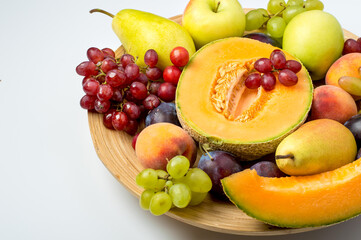 A plate filled with a variety of fruits, melon, apple, pear, grapes and peach on a light background. Top view, horizontal, free copy space.