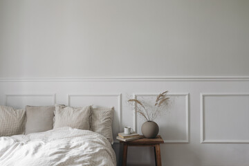 Elegant boho bedroom interior. Vintage wooden bedside table. Round modern vase with dry grass. Cup...