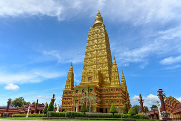 Stunning huge golden pagoda surrounded by beautiful green garden with cloudy blue sky in the temple. Wat Mahathat Wachiramongkhon or Wat Bang Thong, Krabi Province, Thailand.