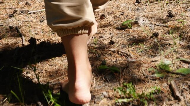 A woman walks barefoot along forest path, feeling soft earth beneath her feet. Tranquility of forest surrounds her as she enjoys beauty of nature. Forest path offers walk into lush forest landscape.