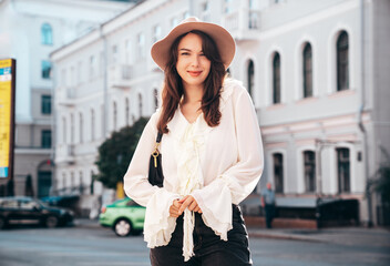 Obraz premium Portrait of young beautiful smiling hipster woman in trendy summer white blouse and jeans. Carefree woman posing in the street in sunny day. Positive model outdoors. Cheerful and happy, closeup
