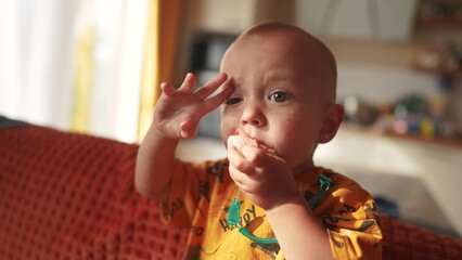 a small newborn sits on the couch with a pacifier in his mouth. happy family childhood dream concept. a little child with a pink pacifier sits and looks at the lifestyle camera baby face close-up