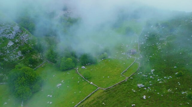 Fog in the spring landscape of pastures and Pasiegas cabins in the Natural Park of the Collados del As&oacute;n. Aerial view from a drone. Hills of Ason Natural Park. Soba Valley, Cantabria, Spain, Europe