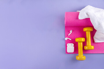Sport and fitness background. Women's sports accessories. yoga mat with dumbbells, bottle of water, towel, jump rope, headphones, on light purple background, copy space