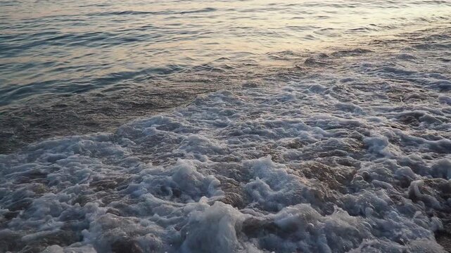 Waves gently lap at shore during stunning sunset over ocean. Golden sunlight reflects off waves as they roll onto shore, creating tranquil atmosphere at sunset by sea. Montenegro summer Canj