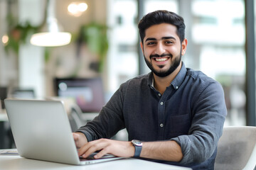 a happy, handsome Middle Eastern businessman working on a laptop at his office desk
