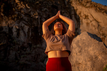 A beautiful plus-size girl is dressed in terracotta-colored sports legging and a cropped top , training sports in a nature, woman  meditates and stretche to maintain a beautiful figure in morning dawn