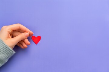 Fototapeta premium A hand delicately holds a vibrant red heart on a soft lavender background