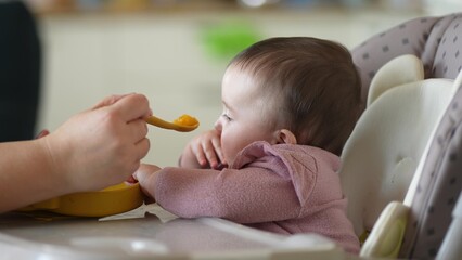 baby newborn eats. happy family dream weaning concept. dirty mess baby girl eating vegetables indoors. baby daughter eats on a feeding chair dirty face. naughty dirty babe indulges while feeding .