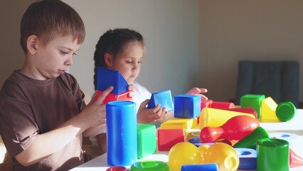 Obraz premium kids girl and baby play in kindergarten. a group of children play toys cubes and cars on the table in kindergarten. happy family preschool education concept. nursery boy baby indoor toddler home