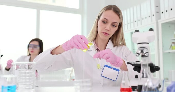 Scientist working in laboratory with microscope and yellow liquid