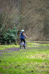 Naklejka premium Rear View of a Young Girl Cycling through a Forest Path in Early Spring