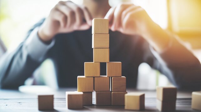 Businessman stacking wooden blocks to build a tall tower on his desk in a contemporary office environment with focus and determination