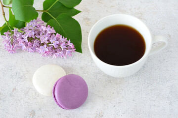 a cup of coffee with white and purple macaroons and lilac flower in the background