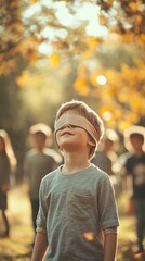 A young boy with eyes covered stands in a sunlit autumn park, surrounded by blurred figures, evoking a sense of mystery and childhood wonder.