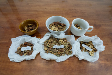 Asian traditional herbs and spices, dried and prepared, shown on a wooden table, on tissue or in cups.