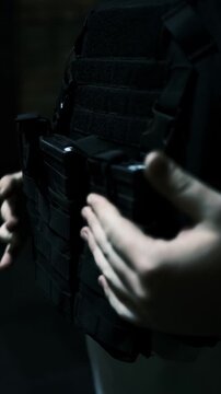 man fastens a black tactical vest around his torso, featuring quick-access magazine pouches close-up captures the focus on readiness, safety efficiency ideal for showcasing tactical preparedness.