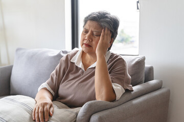 Elderly women feeling dizzy and headache sit on the sofa at home.