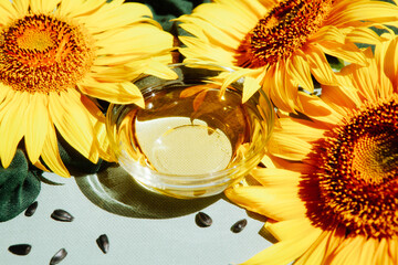 Sunflower oil with yellow sunflowers and black seeds on green background, food ingredient