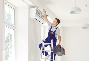 Portrait of professional cheerful smiling electrician man or technician standing on ladder holding...