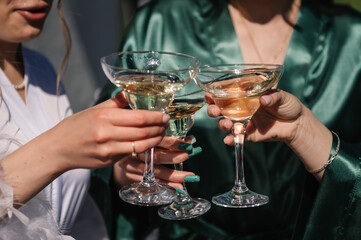 Pretty young ladies friends wear silk robes hold glasses with champagne in hotel. Bride and...