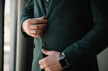 Young beautiful businessman in a black vest and suit closeup. Man fastens the buttons. The groom in a suit. Closeup. The man is buttoning his jacket.
