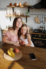 Mother hugging preteen girl with fruit in kitchen at home