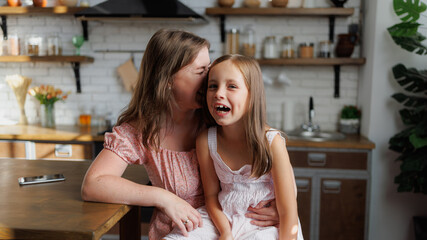 Smiling mother hugging daughter in kitchen at home